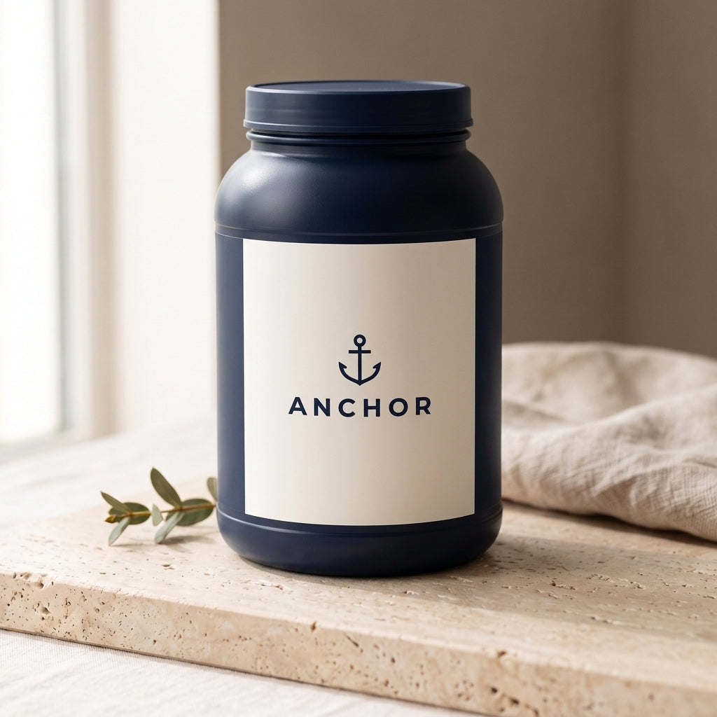 Anchor Whey Protein Isolate Vanilla navy tub on travertine stone with eucalyptus, natural window light
