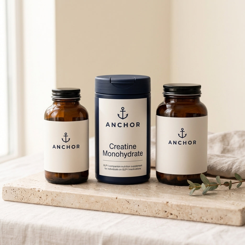 Anchor GLP-1 Companion Bundle amber GLP-1 bottle with navy creatine tub and amber magnesium bottle grouped on travertine stone with eucalyptus, natural window light — Anchor supplement