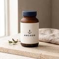 Anchor Magnesium Glycinate navy tub on travertine stone with eucalyptus, natural window light