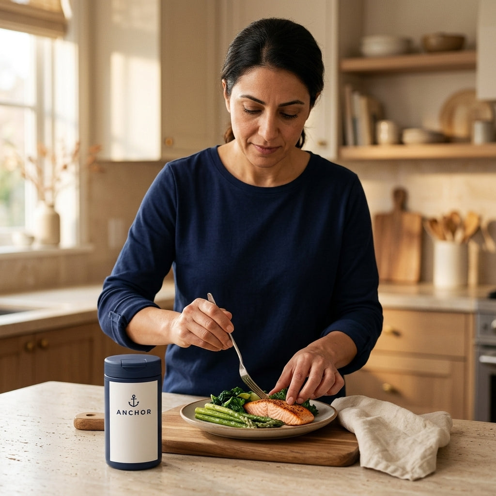 Middle Eastern woman in her 40s plating a salmon and greens lunch with an Anchor digestive enzyme amber bottle on the kitchen counter